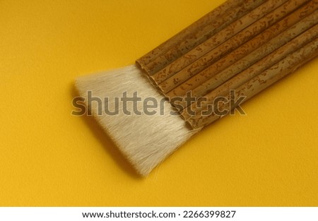 Diagonal cropped view of wooden or bamboo textured handle white brush for cleaning or writing with unusual shape. Object photo isolated on yellow background.