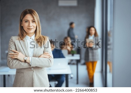 Portrait of young smiling woman looking at camera with crossed arms. Happy girl standing in creative office. Successful businesswoman standing in office with copy space. Urban happy business woman
