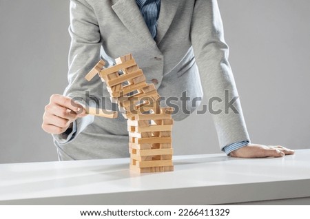 Businesswoman removing wooden block from falling tower on table. Management of risks and economic instability concept with wooden jenga game. Failure and collapse in corporate business Royalty-Free Stock Photo #2266411329