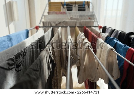 Clean laundry are hanging on the clothesline in a room next to window. so many clean clothes are on the clothesline.  Royalty-Free Stock Photo #2266414711