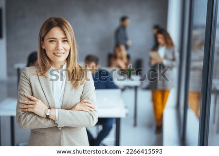 Successful businesswoman standing in creative office and looking at camera. Young woman entrepreneur in a coworking space smiling. Portrait of beautiful business woman standing