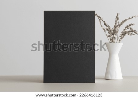 Black invitation card mockup with a lavender decoration on the beige table. 5x7 ratio, similar to A6, A5.