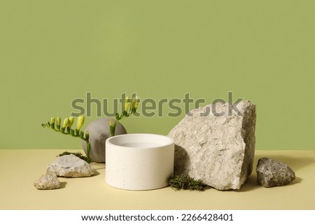 Plaster podium, stones and freesia flowers on green background