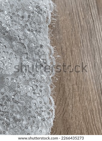 Close-up of textured embroidery with lace and shiny sequins on a wedding dress on a wooden background