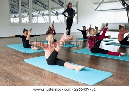 Strength and balance exercises. Group of little girls, children, gymnasts training with female coach indoors. Concept of sportive lifestyle, childhood, education, health, professional sport. Royalty-Free Stock Photo #2266439751