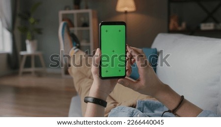 Close up shot of hands of guy who lies on couch using smart phone with chroma key green screen - a perfect template for your content