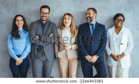 Multi-ethnic group of people in formal businesswear standing in a row. Group of business persons standing against a wall. Studio shot of a group of people waiting in a line against a gray background
