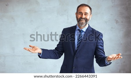 Mature cheerful executive businessman at workspace office. Portrait of smiling ceo at modern office workplace in suit looking at camera. Happy leader standing in front of company building