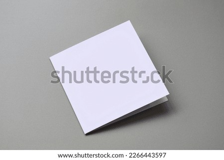 Laying blank empty folded square greeting card mock up on clean cool grey background with copy space. For use as a Christmas, birthday, wedding or celebration background template. Royalty-Free Stock Photo #2266443597