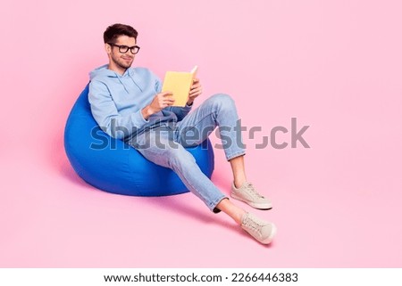 Photo of concentrated focused clever man sitting cozy bag reading favorite book near empty space isolated on pink color background