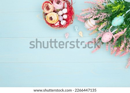 Easter composition of pink spring flowers, colorful roses, cute bunnies and decorative eggs in a nest. Content for Easter holiday on blue wooden background. Flat lay, top view, close up, copy space