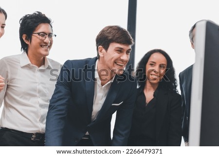 A team of exclusive diversity businesspeople are gathered together in an office, excitedly watching their accomplishment on a laptop computer. Idea for fostering strong teamwork in the workplace.
