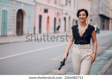 Portrait of a beautiful smiling female in stylish office clothes walking down the street while holding an umbrella in her hand. Business woman style. Fashion photo.