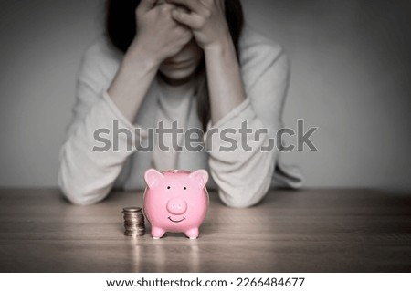 Sad girl leaned on the table, covering her face with hands, in the foreground a cute pink piggy bank. Woman lost her savings, was fired, and is experiencing financial difficulties, feels depressed. Royalty-Free Stock Photo #2266484677