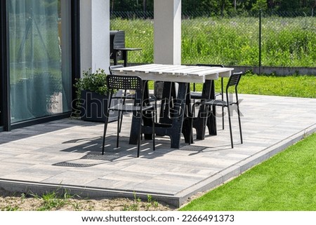 Terrace table made of white pallet standing on plastic trestles, black plastic chairs.