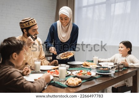 African american woman in hijab serving food on plate near family and ramadan dinner Royalty-Free Stock Photo #2266497783