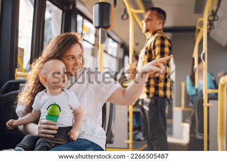Young plus size mother in casual wear holding little toddler boy in her lap and together looking at window. Mom and her child enjoying a bus journey together. Mother pointing her finger. Copy space. Royalty-Free Stock Photo #2266505487