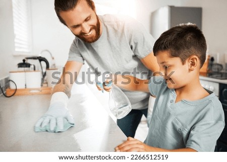 Father teaching young son cleaning chores in the family home having fun and bonding together. Smiling and loving father helping, washing and wiping kitchen counter with his little boy indoors Royalty-Free Stock Photo #2266512519