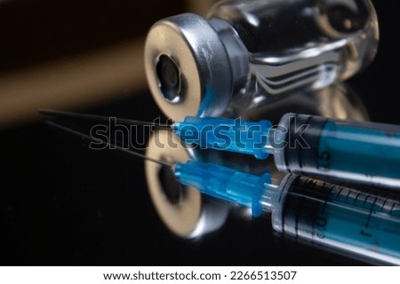 The vial with the dose of the vaccine lies next to the syringe on the mirror. The vial and syringe with the vaccine are reflected in the surface of the black mirror. The concept of vaccination.