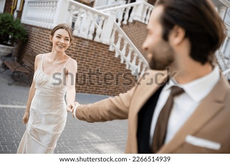 blurred groom in suit holding hand of happy bride in white dress