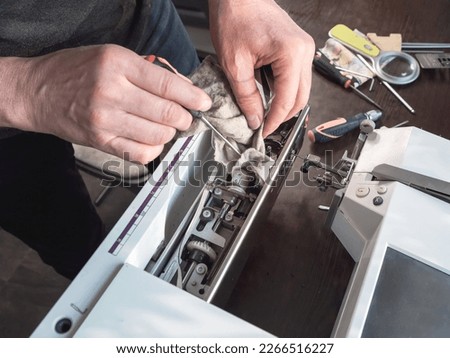 Master repairs the sewing machine. Internal cleaning of the mechanism. Professional adjustment of a sewing machine in a small factory. Cleaning and repair of professional equipment. Royalty-Free Stock Photo #2266516227