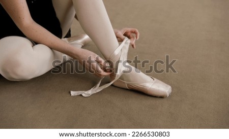 Ballerina in training bodysuit takes off her pointe shoes after stretching and gymnastic workout in dance studio. Female ballet dancer finished preparing for performance. Classic ballet dance school. Royalty-Free Stock Photo #2266530803