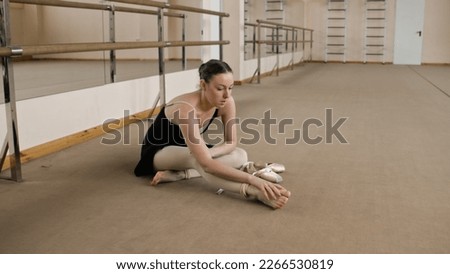 Female ballet dancer finished choreography rehearsal. Tired ballerina in training bodysuit takes off pointe shoes after stretching and gymnastic workout in dance studio. Classic ballet dance school. Royalty-Free Stock Photo #2266530819