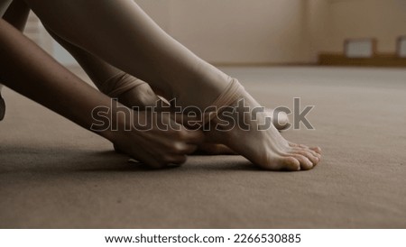 Close up shot of ballerina taking off her pointe shoes after stretching and gymnastic workout in dance studio. Female ballet dancer finished preparing for performance. Classical ballet dance school. Royalty-Free Stock Photo #2266530885