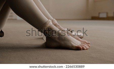 Close up shot of ballerina taking off her pointe shoes after stretching and gymnastic workout in dance studio. Female ballet dancer finished preparing for performance. Classical ballet dance school. Royalty-Free Stock Photo #2266530889