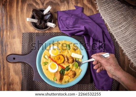 Top view of a plate of fanesca with one hand taking a portion with a spoon on a wooden background Royalty-Free Stock Photo #2266532255