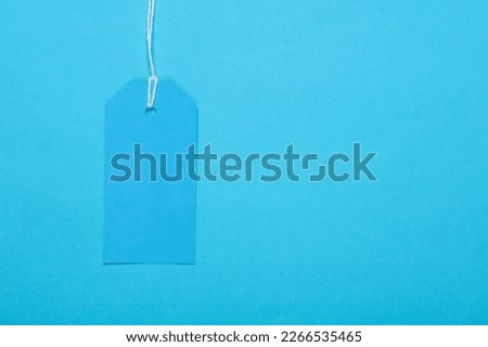 Blue blank clothing price tag or label mockup with string on blue background. Sale, shopping concept. Top view