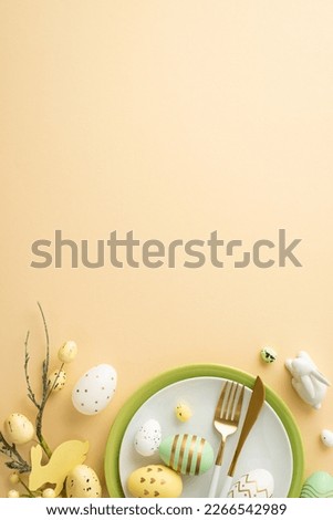 Easter decorations concept. Top view vertical photo of plates cutlery white green yellow easter eggs ceramic bunny and easter plant on isolated pastel beige background with copyspace
