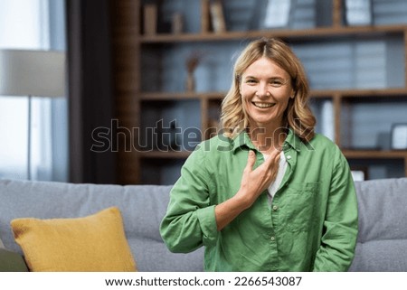 Smiling senior beautiful young woman sitting on sofa at home in front of camera and speaking in sign language.