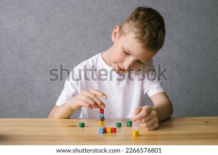 Cute boy plays with multicolored playing dice for board game, builds a tower up Royalty-Free Stock Photo #2266576801