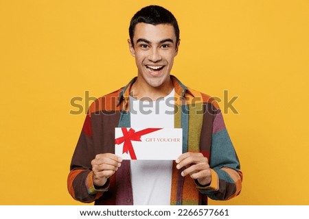 Young happy middle eastern man 20s he wear casual shirt white t-shirt hold gift certificate coupon voucher card for store isolated on plain yellow background studio portrait People lifestyle concept