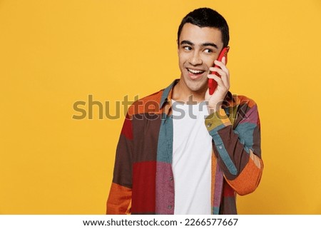 Young fun middle eastern man 20s he wear casual shirt white t-shirt talk speak on mobile cell phone conducting pleasant conversation isolated on plain yellow background studio People lifestyle concept