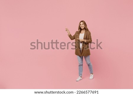 Full body young fun successful employee business woman 30s she wear casual brown classic jacket point index finger aside on workspace area mock up isolated on plain pastel light pink background studio Royalty-Free Stock Photo #2266577691