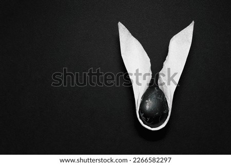 Decorative rabbit ears with an egg on a dark textured background. Celebrate Easter, do it yourself, flat lay. Minimalist style. Banner, copy space.