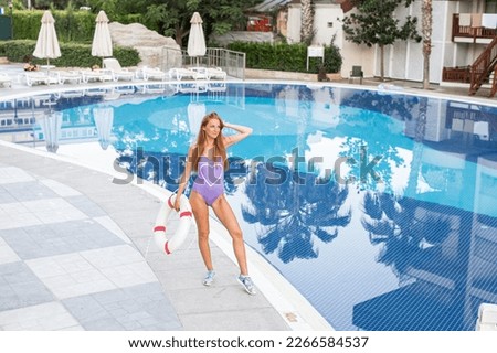 Close-up selfie-portrait of attractive girl with long hair standing near pool. She is smiling to the camera and shows cool look. Straw hat on head. On resort, holiday, vacation.