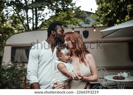 Mixed race family with dark skinned infant daughter spend time together hugs and kisses in camper park. African american man his fair skin wife and little girl enjoying summer vacation in open air Royalty-Free Stock Photo #2266593219
