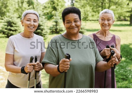 Waist up portrait of three sportive senior women smiling at camera holding walking poles outdoors Royalty-Free Stock Photo #2266598983
