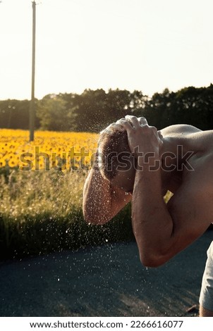boy washes himself against the background of a sunflower field on a hot summer day