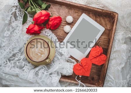 Сomposition with red rose flowers bouquet, cup of coffee, paper hearts and e-reader on wooden tray. Template for feminine blog social media. Valentines day, Mothers day greeting.