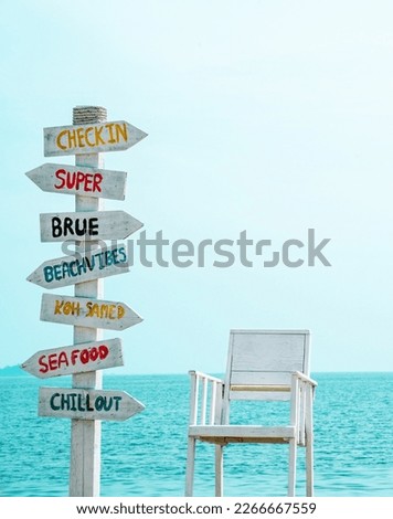 Funny multicolored direction signs pointing everywhere on a tropical beach against the background of the sea. Nearby there is a wooden beach chair, painted white