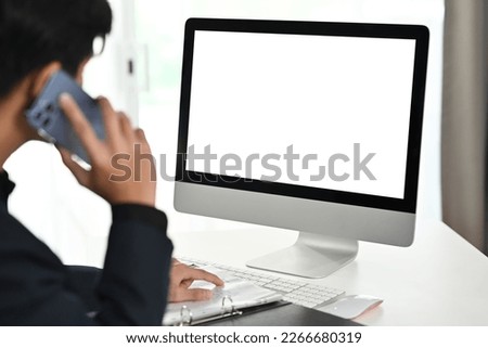Cropped image of young male investor having phone conversation and looking at computer monitor at office desk