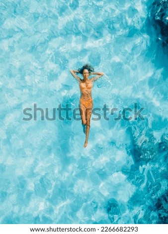 Beautiful woman floating in transparent blue ocean. Aerial view, top view.