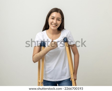 Happy young asian woman broken arm and leg on isolated. Woman put on plaster cast splint with walking sticks crutches. Patient wearing sling support arm with neck collar. life insurance and accident Royalty-Free Stock Photo #2266700193