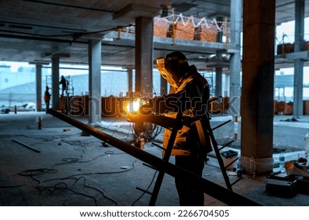 A builder in a protective suit performs welding work on metal. Construction of an industrial building Royalty-Free Stock Photo #2266704505