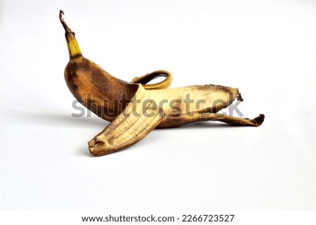 On a white background lies a banana that has not been completely peeled. The banana peel has dark spots. The banana is overripe. Royalty-Free Stock Photo #2266723527