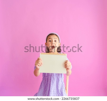 Pretty little girl holding a blank notebook with a surprised face. 